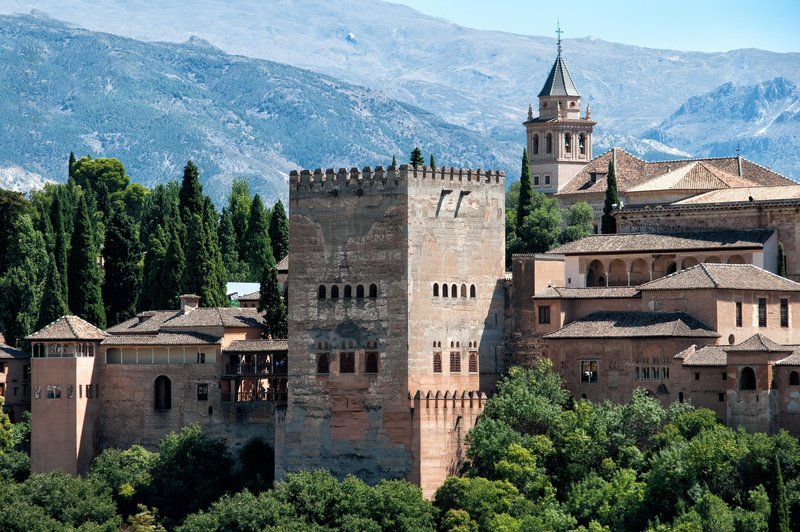 Torre de Comares in der Alhambra von Granada vor der Sierra Nevada, umgeben von maurischer Palastarchitektur und der Kirche Santa María de la Alhambra