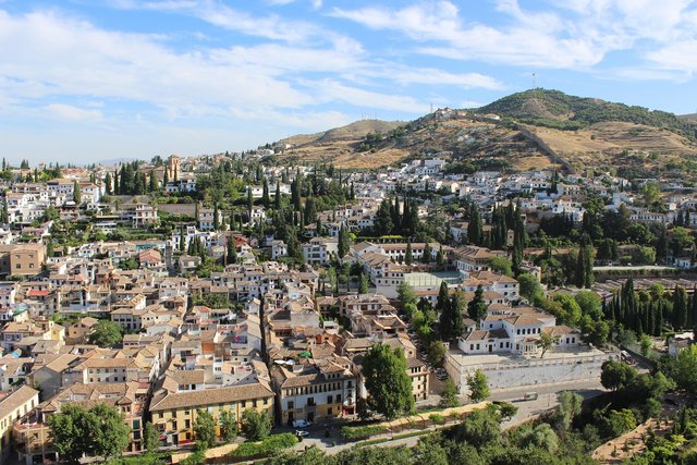 Blick auf das maurische Viertel Albaicín in Granada mit weiß getünchten Häusern und der alten Stadtmauer Muralla Zirí, die sich den Hügel von San Miguel Alto hinaufzieht