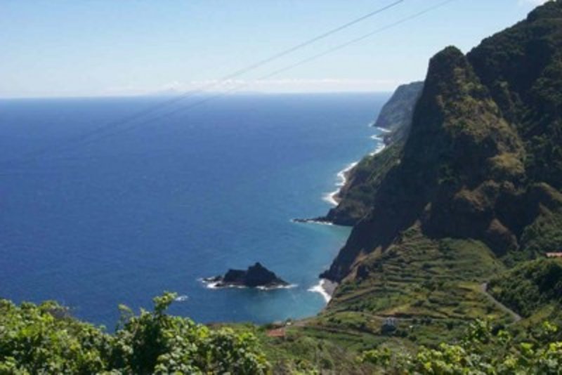 Blick auf die wilde Nordwestküste Madeiras mit terrassierten Feldern, steilen Klippen und vorgelagerten Felsen im Atlantik.