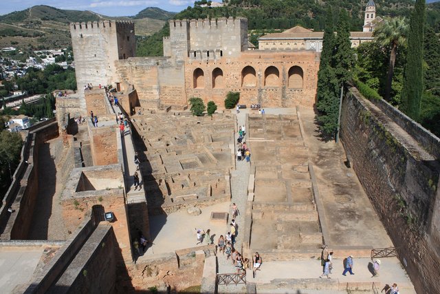 Blick auf die Alcazaba der Alhambra in Granada mit Ruinen alter Gebäudegrundrisse, Touristenwegen und dem markanten Torre de la Vela im Hintergrund.