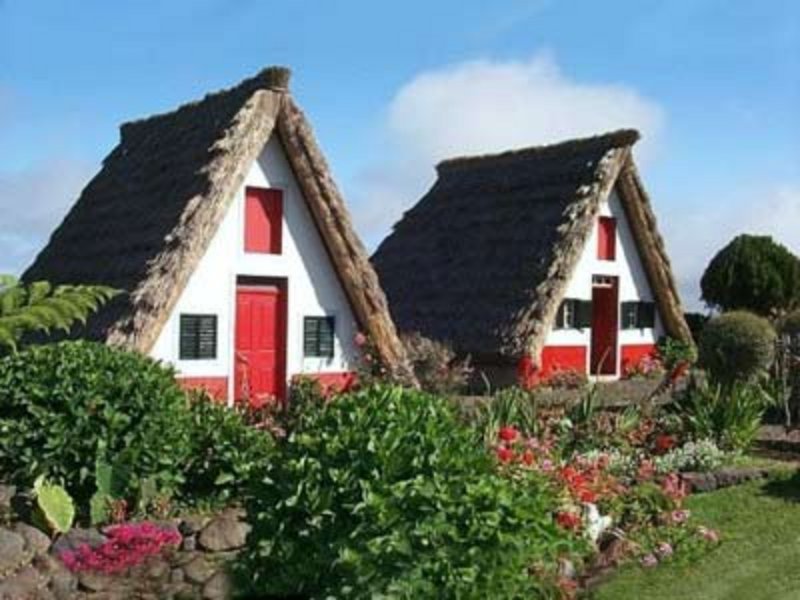 Traditionelle Santana-Häuser auf Madeira – strohgedeckte Dreieckshäuser mit farbenfrohen Fassaden inmitten blühender Gärten.