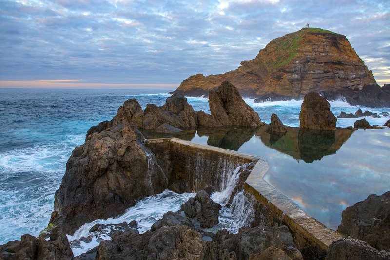 Natürlichen Lavabecken, die zu den Piscinas Naturais de Porto Moniz gehören – eines der beliebtesten Highlights im Nordwesten Madeiras. Im Hintergrund ist der markante Ilhéu Mole zu sehen, die vorgelagerte Felseninsel mit kleinem Leuchtturm bzw. Signalpunkt oben drauf.